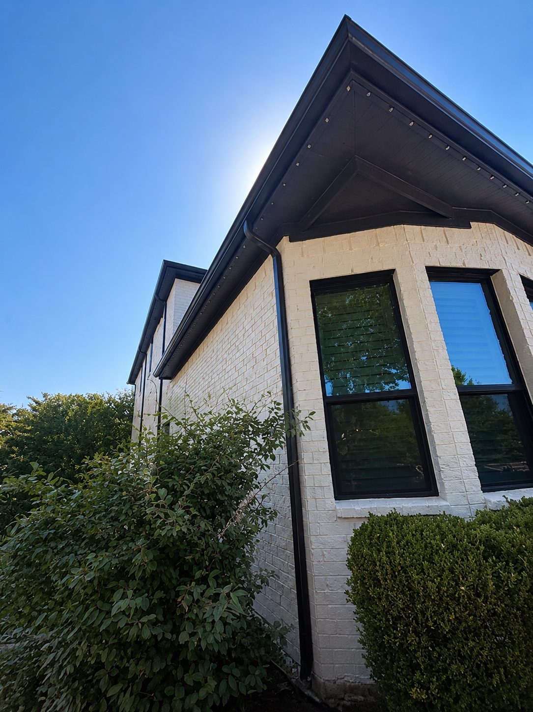 Black downspout and fascia detail on a white brick home
