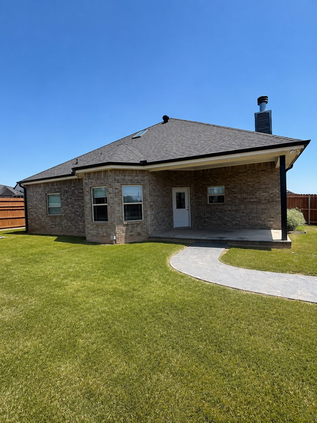 Rear of a brick home with new white seamless gutters and a curved concrete walkway