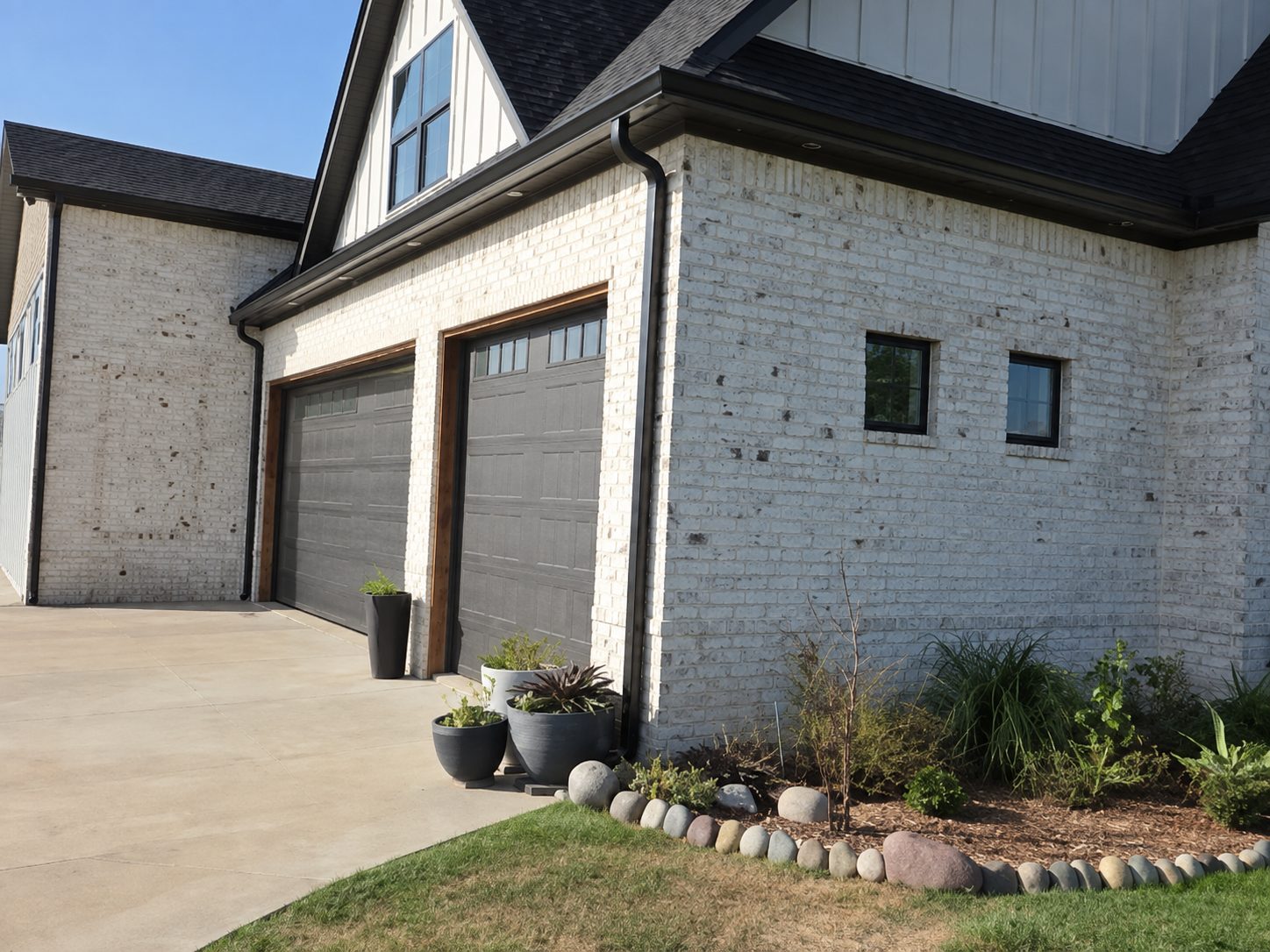 Black 5-inch gutters and downspouts on a painted white brick modern home.