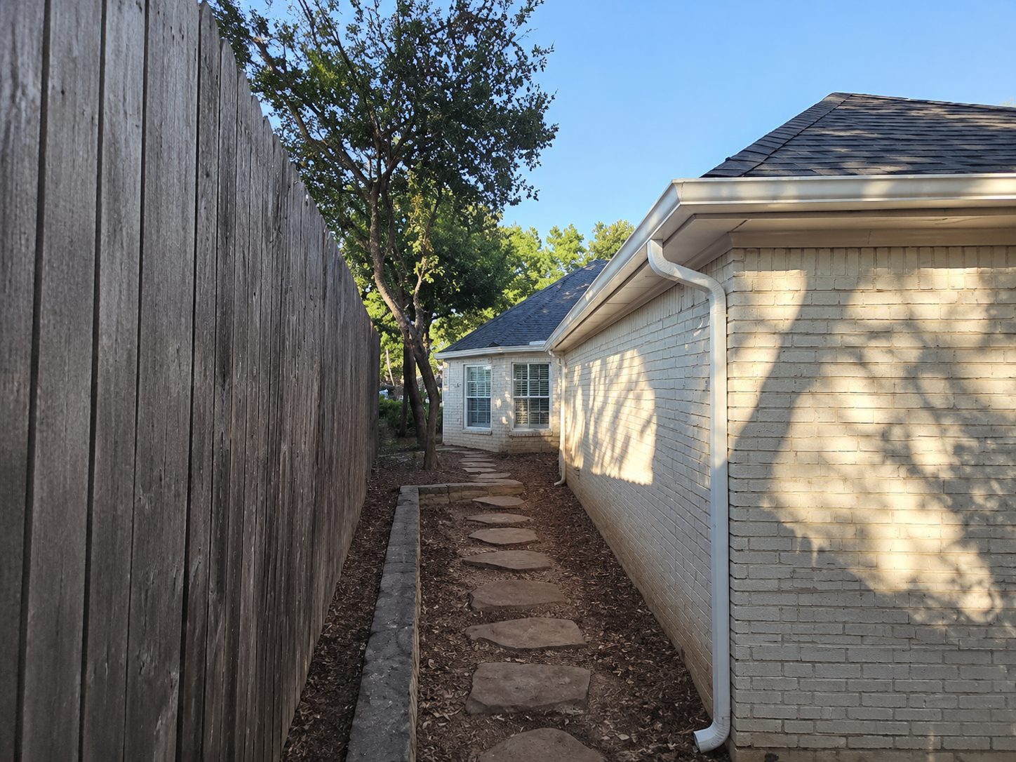 White downspout on a painted brick home along a narrow side yard