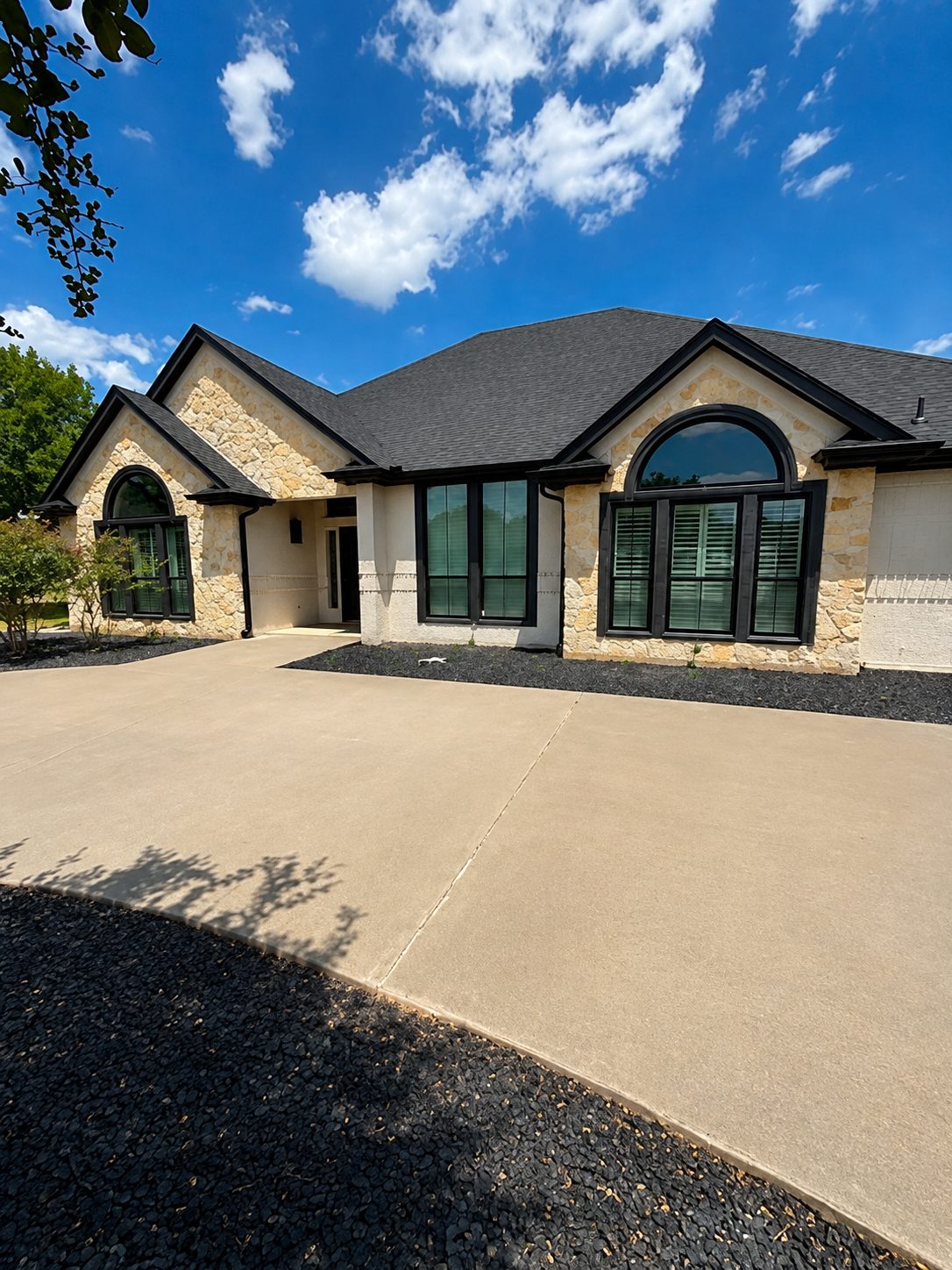 Stone home, black gutters, downspouts tucked to the corners along the drive.