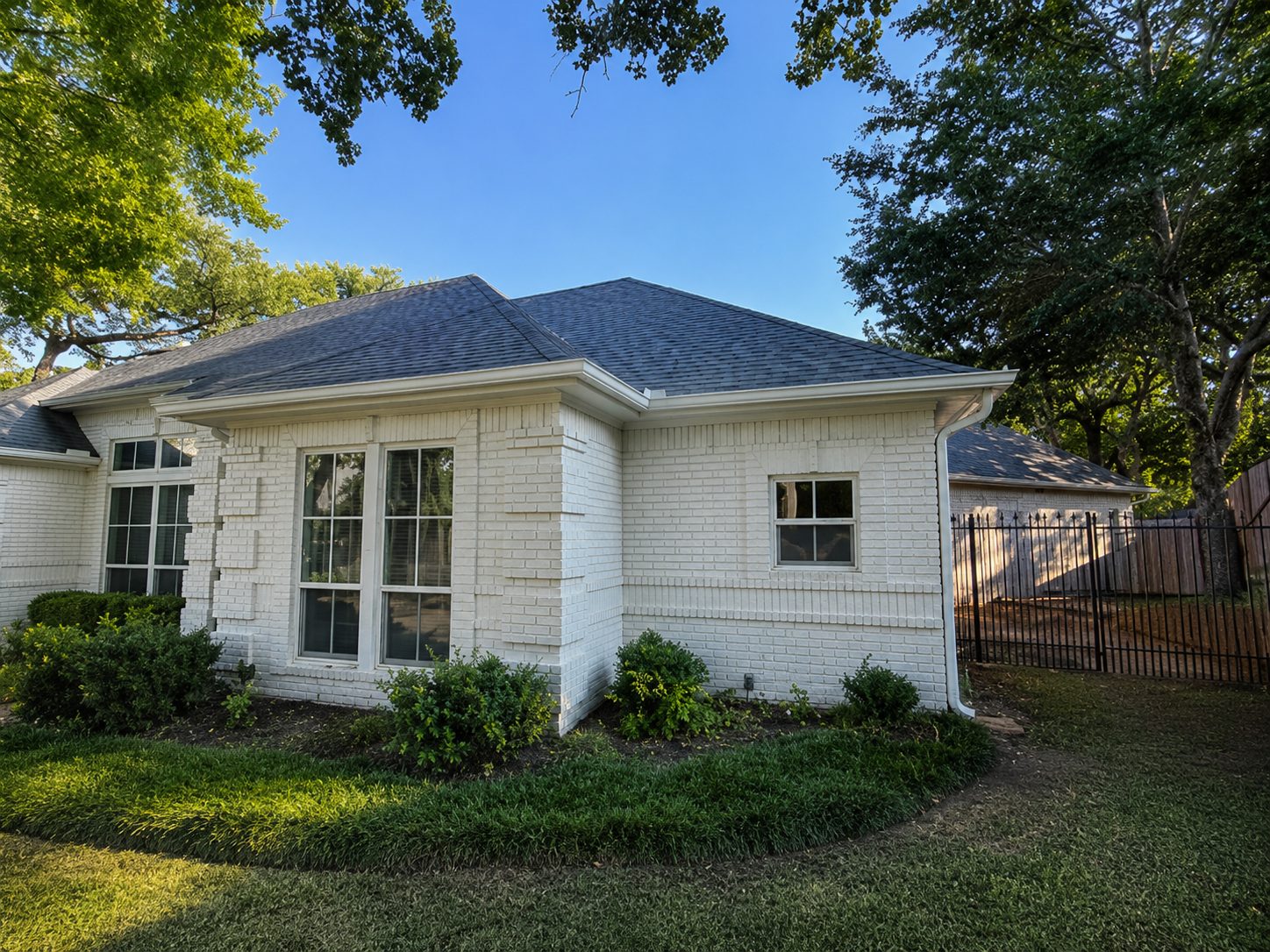 White seamless gutters on a painted brick ranch with bay windows.