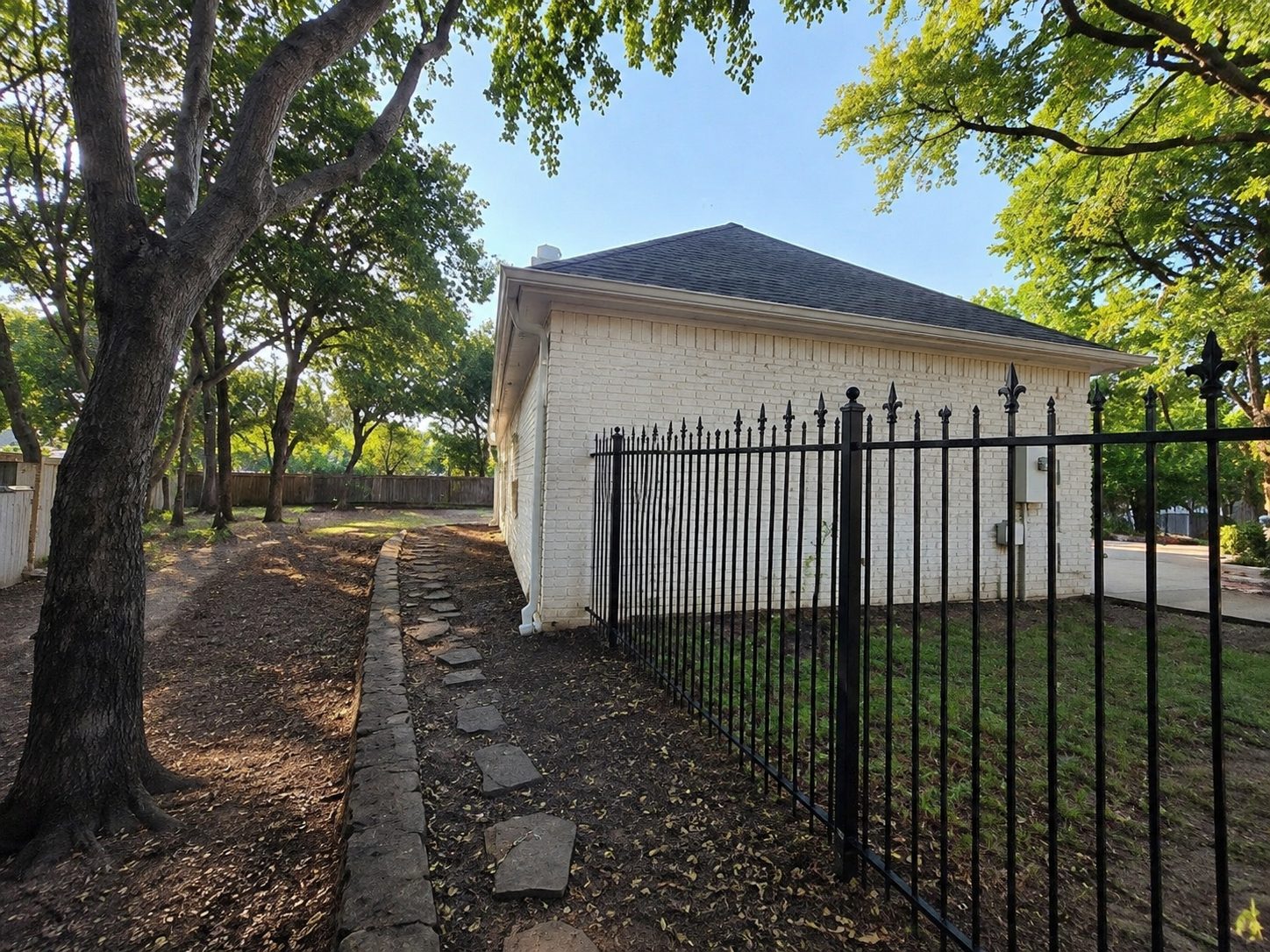 Downspout and side-yard drainage on a white brick home with iron fencing.