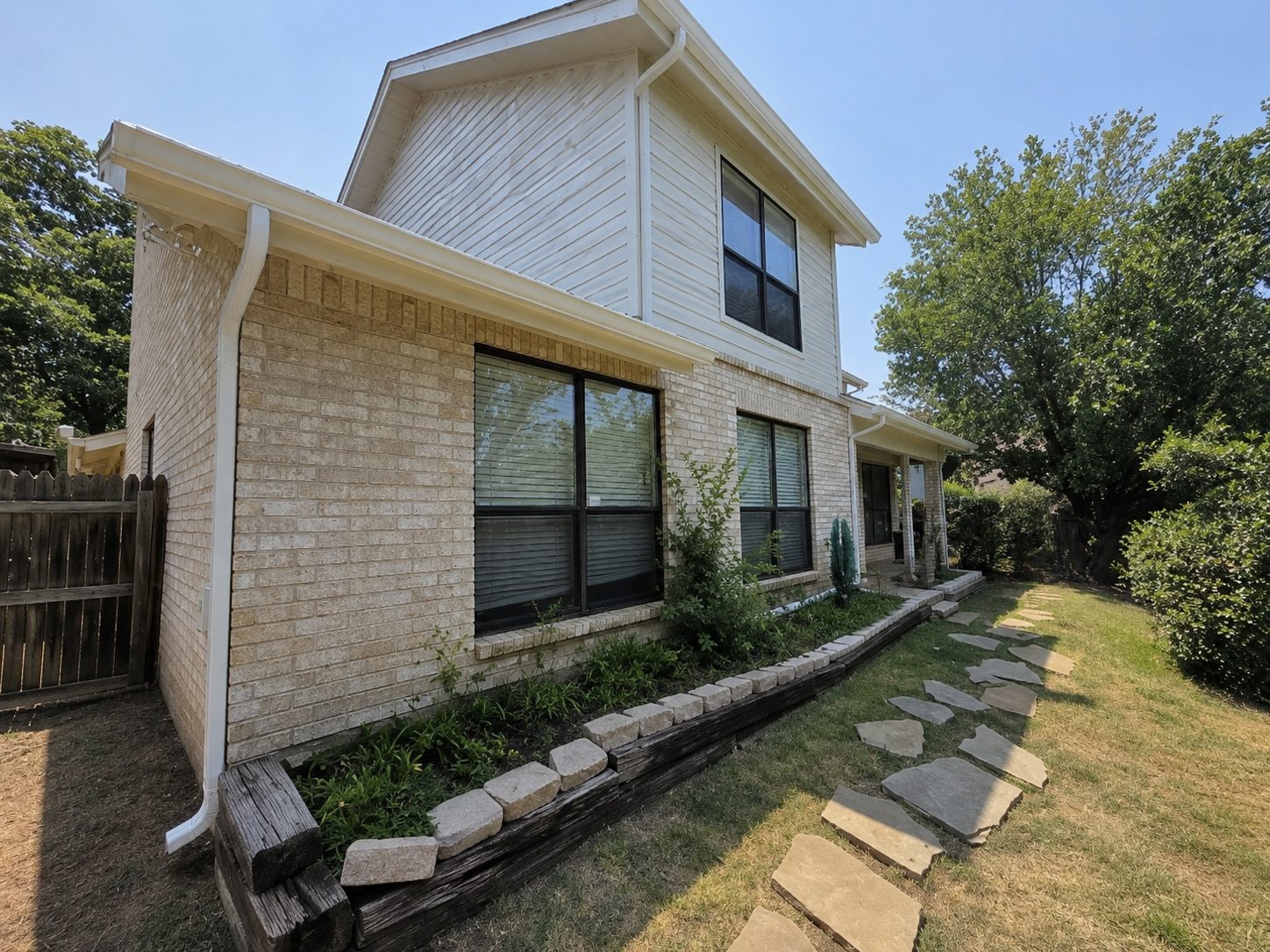 White gutters and a full-height downspout on a two-story painted brick home.